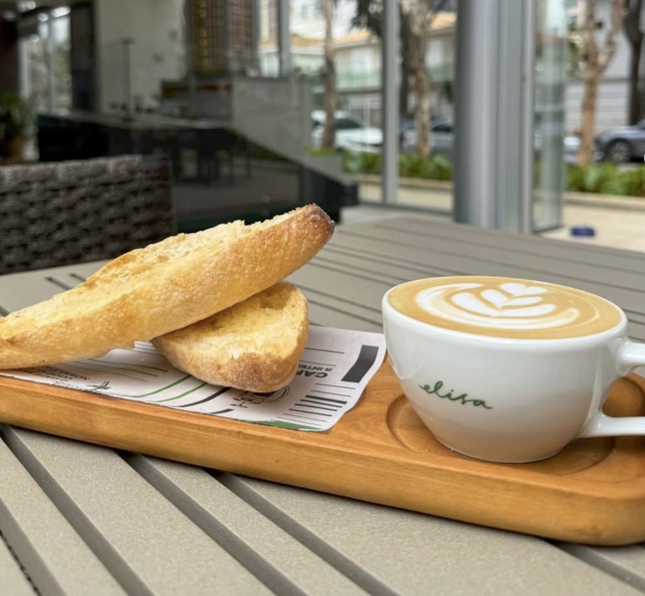 A branded latte and fresh baked bread on a wooden board at Elisa Café e Torrefação
